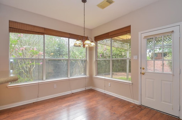 unfurnished dining area with baseboards, visible vents, a chandelier, and wood finished floors