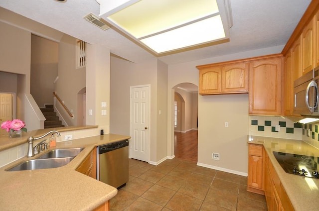 kitchen featuring arched walkways, a sink, stainless steel appliances, light countertops, and backsplash