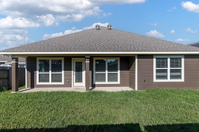 rear view of property with a shingled roof, a lawn, and fence