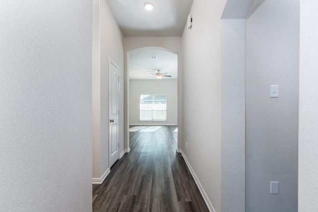 hall with arched walkways, dark wood-style flooring, visible vents, and baseboards