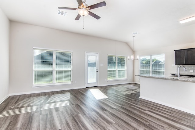 unfurnished living room featuring ceiling fan with notable chandelier, dark wood-type flooring, a sink, visible vents, and vaulted ceiling