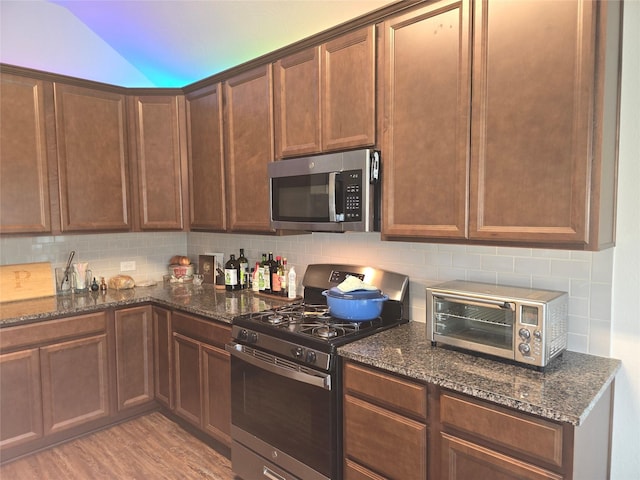 kitchen featuring light wood finished floors, a toaster, appliances with stainless steel finishes, and backsplash