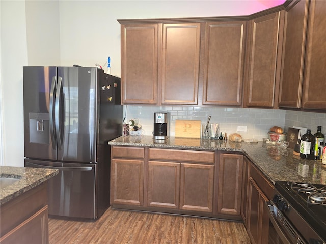 kitchen featuring stainless steel appliances, dark stone counters, decorative backsplash, and wood finished floors