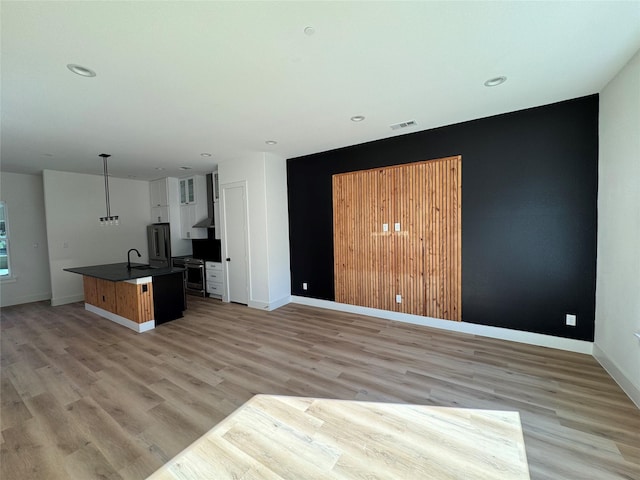 interior space with wall chimney range hood, sink, light hardwood / wood-style floors, white cabinets, and a center island with sink