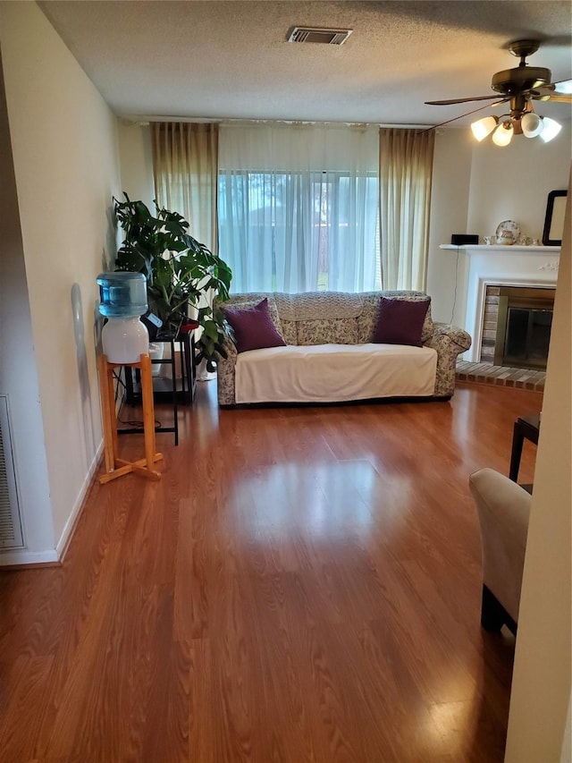 living area featuring a fireplace, visible vents, a ceiling fan, a textured ceiling, and wood finished floors