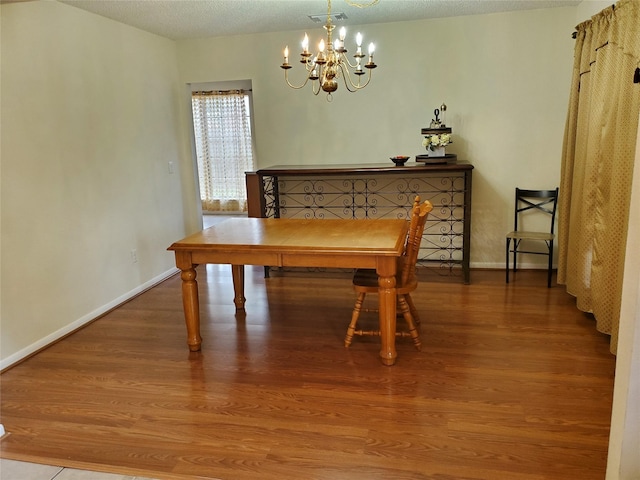 dining space with a textured ceiling, a notable chandelier, wood finished floors, visible vents, and baseboards