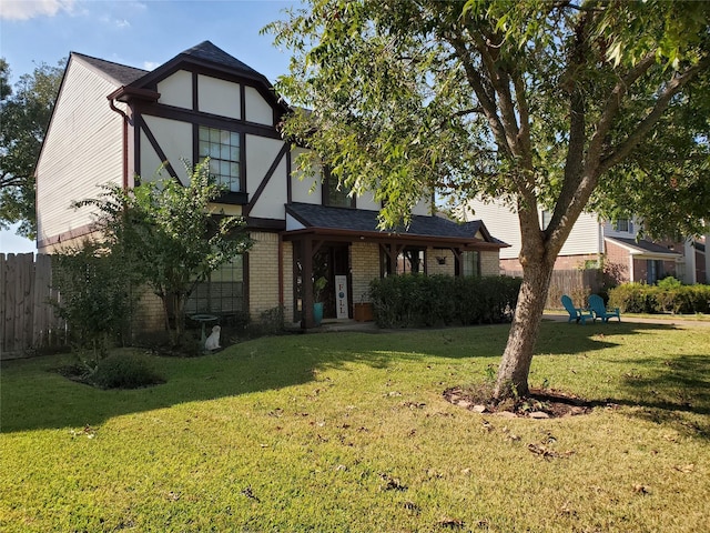 english style home with brick siding, a front yard, and fence