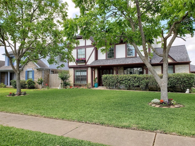 tudor house featuring brick siding, a front yard, and a shingled roof