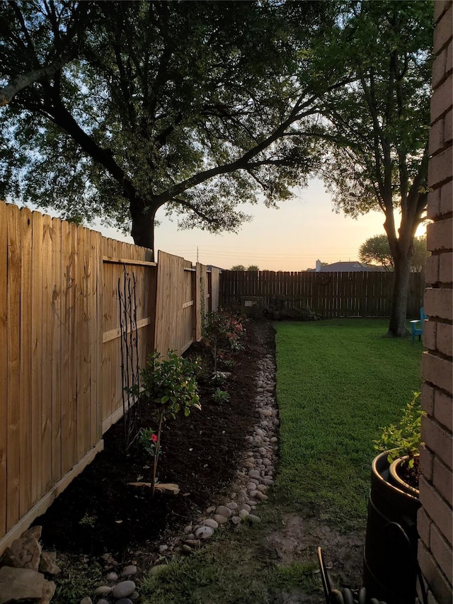 yard at dusk featuring a fenced backyard