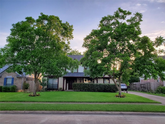 view of front of property with brick siding, roof with shingles, fence, and a yard