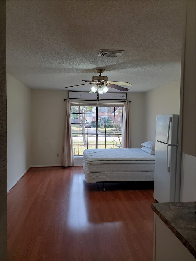 unfurnished bedroom featuring ceiling fan, a textured ceiling, visible vents, freestanding refrigerator, and dark wood-style floors