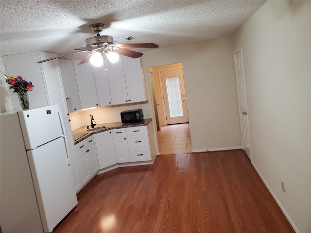 kitchen featuring black microwave, wood finished floors, freestanding refrigerator, a textured ceiling, and white cabinetry