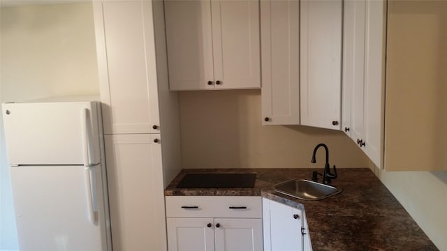 kitchen with dark countertops, cooktop, freestanding refrigerator, white cabinetry, and a sink