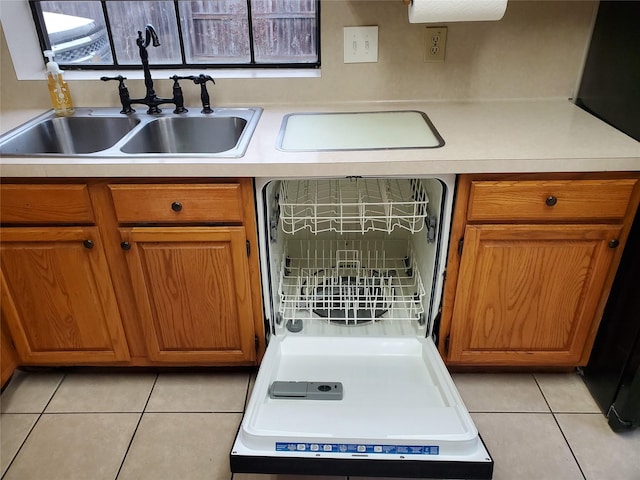 kitchen featuring brown cabinets, light tile patterned floors, light countertops, a sink, and dishwashing machine