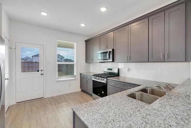 kitchen featuring appliances with stainless steel finishes, a sink, light wood-style flooring, and light stone countertops