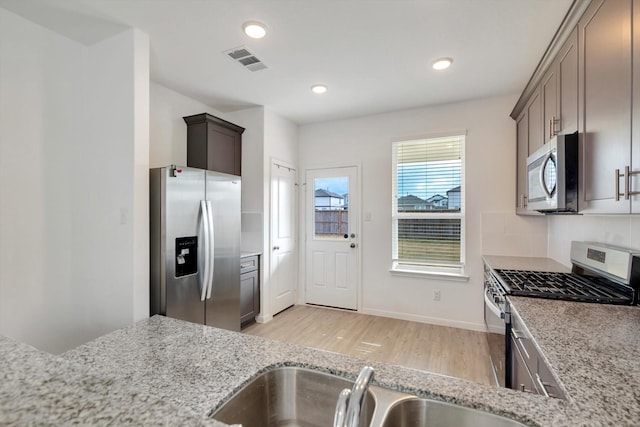 kitchen with stainless steel appliances, light wood-type flooring, visible vents, and light stone countertops