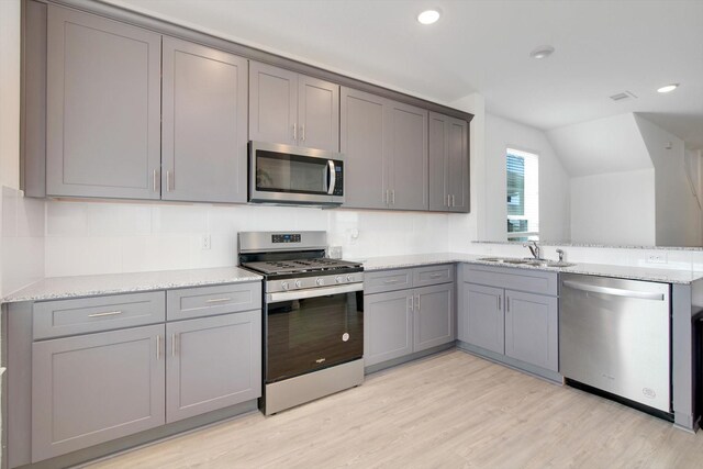 kitchen with light wood finished floors, appliances with stainless steel finishes, vaulted ceiling, gray cabinets, and a sink