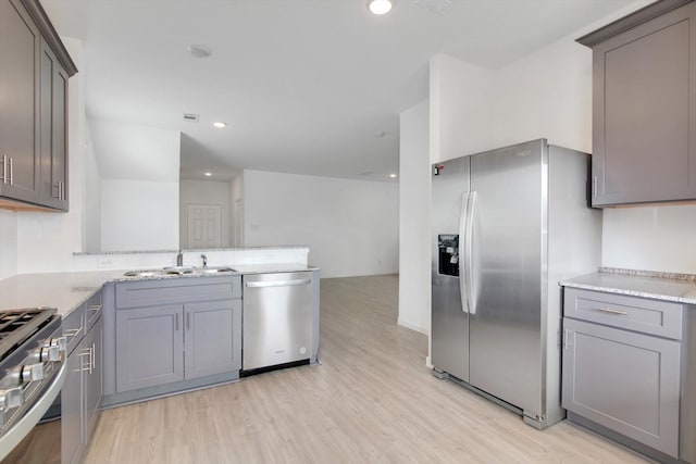 kitchen with appliances with stainless steel finishes, gray cabinets, a sink, and light wood-style floors