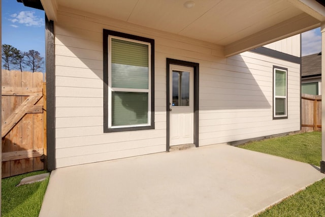 view of exterior entry with fence and a patio