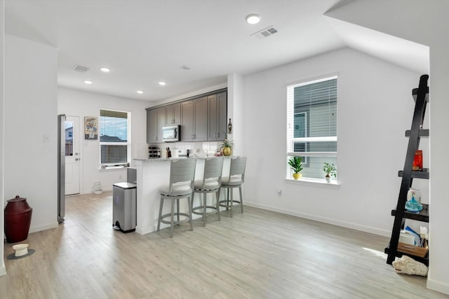 kitchen with light wood-style floors, visible vents, stainless steel microwave, and a breakfast bar area