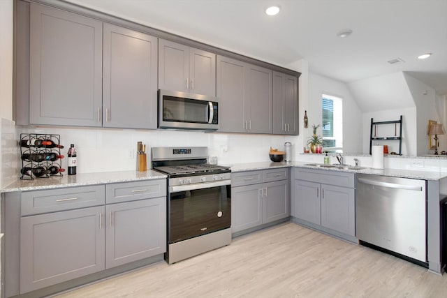 kitchen featuring appliances with stainless steel finishes, light wood-type flooring, a sink, and gray cabinetry