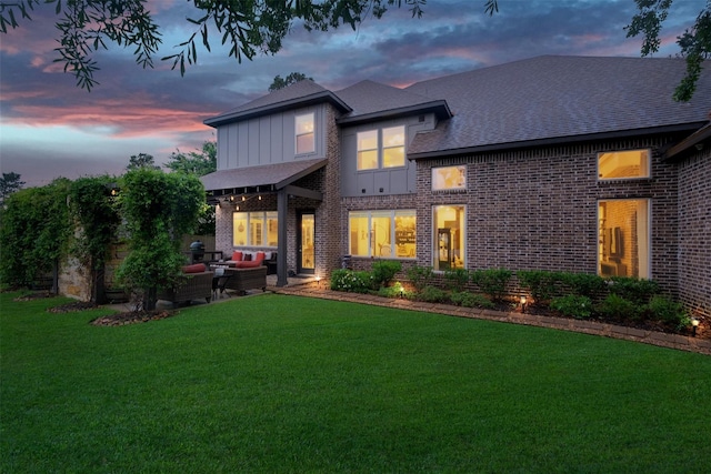 back house at dusk featuring a yard and outdoor lounge area