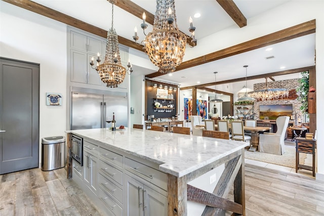 kitchen with decorative light fixtures, a center island with sink, light wood-type flooring, gray cabinets, and beam ceiling