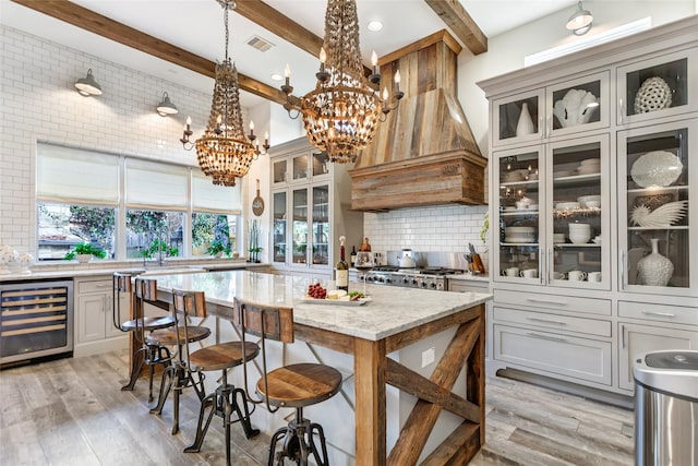 kitchen featuring decorative light fixtures, beverage cooler, backsplash, stove, and light stone countertops