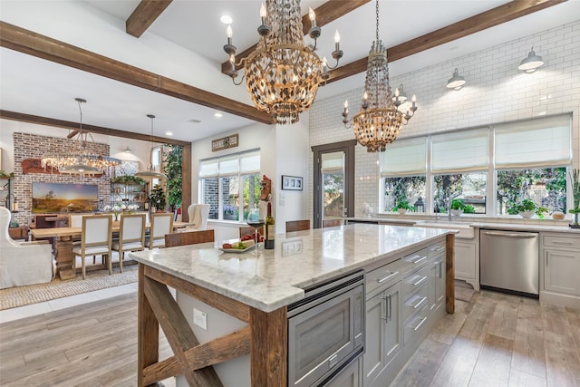 kitchen with appliances with stainless steel finishes, decorative light fixtures, beamed ceiling, a chandelier, and light stone counters