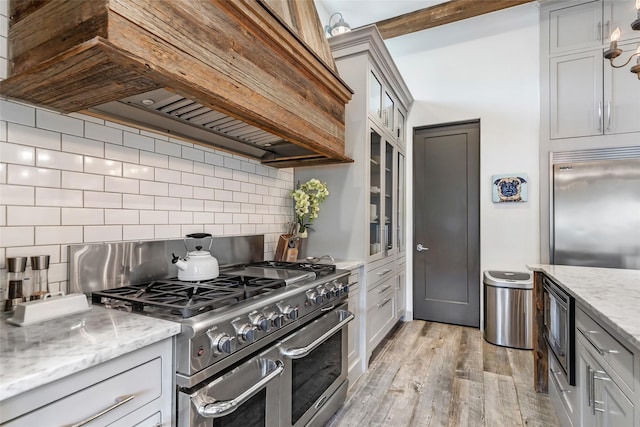 kitchen with built in appliances, light stone countertops, custom exhaust hood, and light wood-type flooring