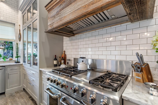 kitchen featuring light stone counters, decorative backsplash, stainless steel appliances, and custom exhaust hood