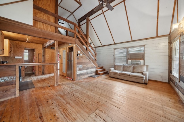 unfurnished living room with ceiling fan, high vaulted ceiling, light hardwood / wood-style flooring, and wood walls