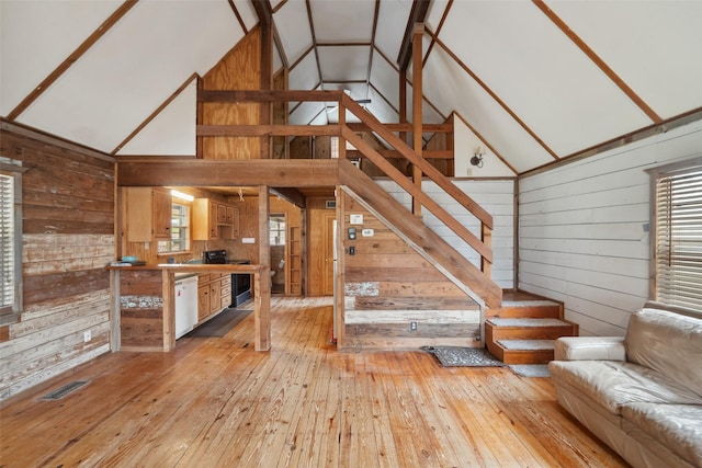 unfurnished living room featuring high vaulted ceiling, wooden walls, and light hardwood / wood-style floors