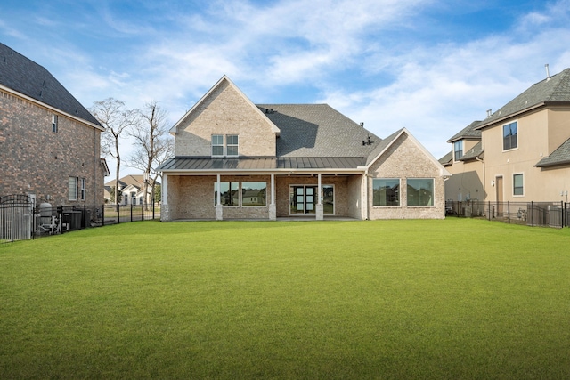 back of property with a standing seam roof, brick siding, a lawn, and a fenced backyard