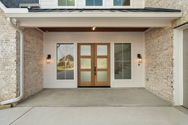 property entrance featuring french doors, brick siding, and a standing seam roof