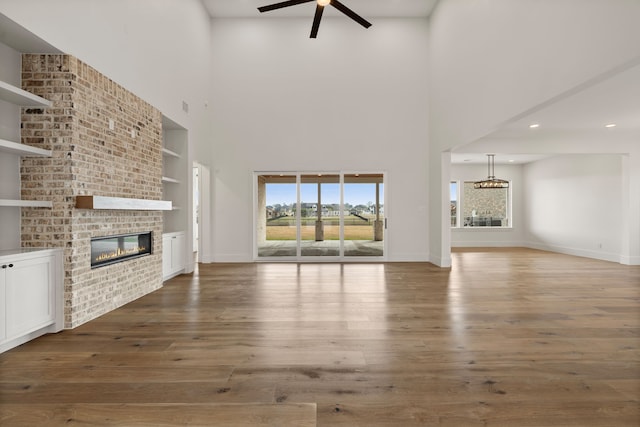 unfurnished living room featuring built in shelves, wood finished floors, a ceiling fan, baseboards, and a brick fireplace