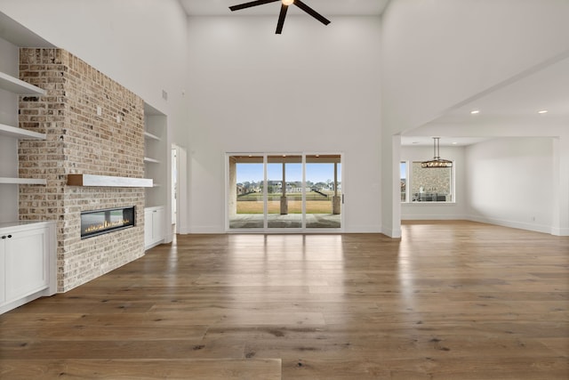 11585 Grandview Dr, Montgomery, TX 77356 - unfurnished living room featuring built in shelves, a ceiling fan, a brick fireplace, a towering ceiling, and wood finished floors