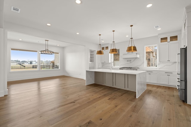 kitchen with high end refrigerator, a sink, white cabinets, backsplash, and light wood finished floors