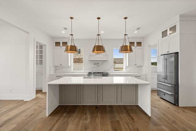 kitchen featuring tasteful backsplash, a kitchen island with sink, high end refrigerator, and wood finished floors