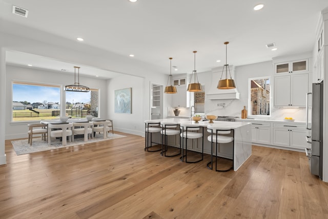 kitchen with high end refrigerator, white cabinetry, light wood finished floors, an island with sink, and a kitchen bar