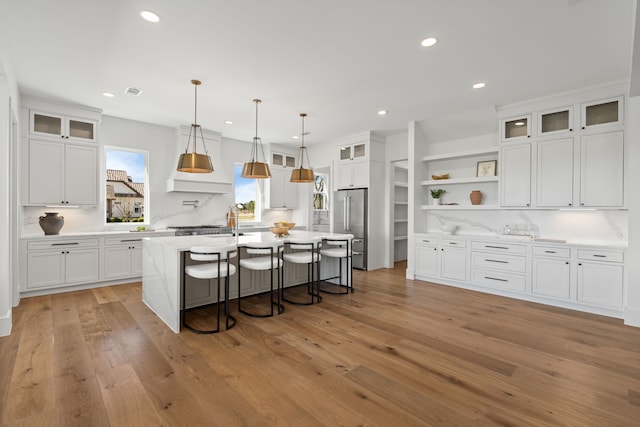 kitchen featuring high end refrigerator, white cabinetry, open shelves, and a center island with sink