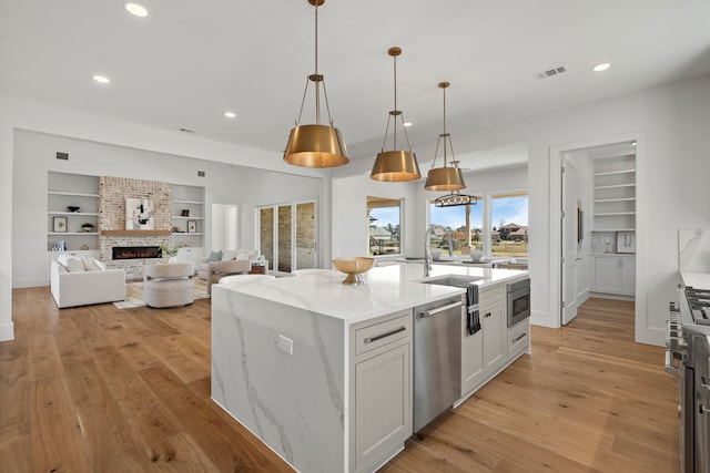 kitchen featuring light wood finished floors, visible vents, appliances with stainless steel finishes, built in shelves, and a fireplace