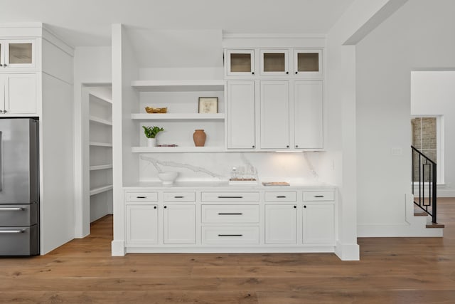 kitchen with glass insert cabinets, white cabinetry, stainless steel refrigerator, and wood finished floors