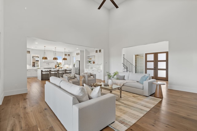 living area with french doors, stairway, a high ceiling, hardwood / wood-style floors, and baseboards