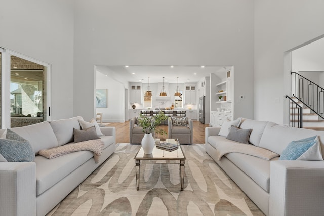 living room with light wood-style floors, recessed lighting, a towering ceiling, and stairs