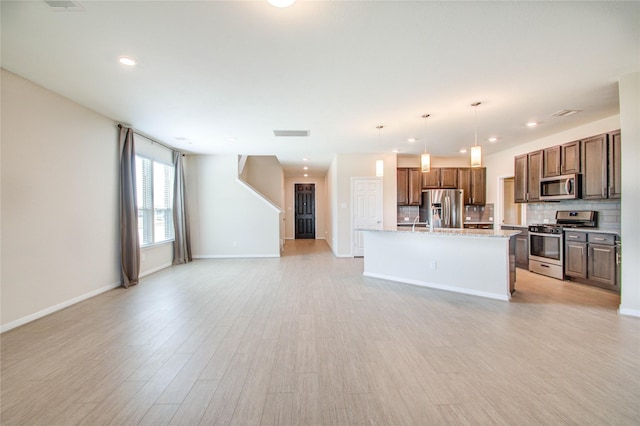 kitchen featuring tasteful backsplash, stainless steel appliances, decorative light fixtures, and an island with sink