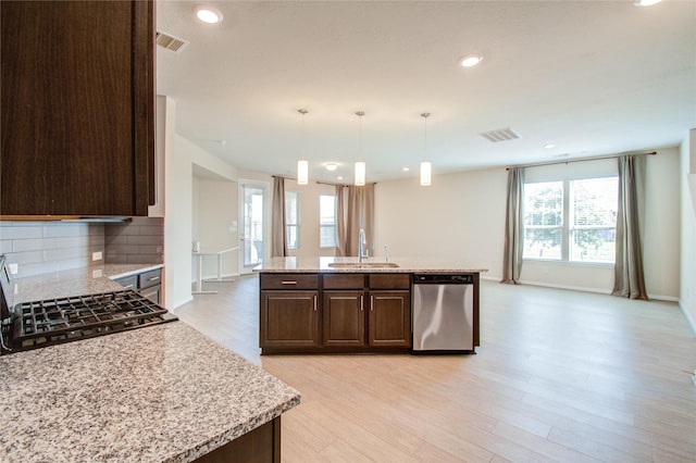 kitchen featuring light stone countertops, sink, stainless steel dishwasher, and decorative light fixtures