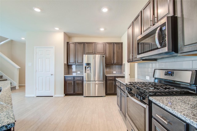 kitchen featuring appliances with stainless steel finishes, light stone counters, backsplash, and dark brown cabinetry