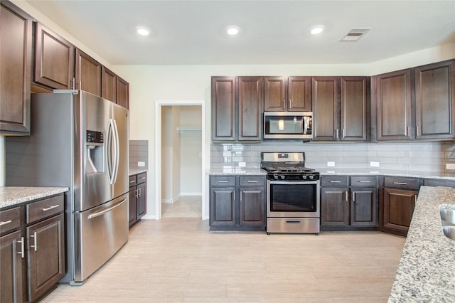 kitchen with light stone counters, decorative backsplash, dark brown cabinets, and stainless steel appliances