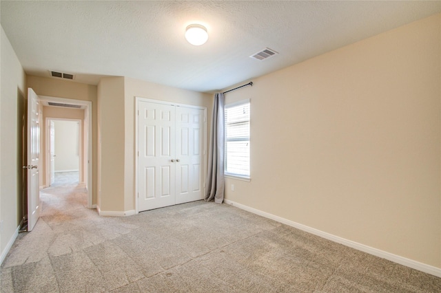 unfurnished bedroom with light colored carpet, a closet, and a textured ceiling